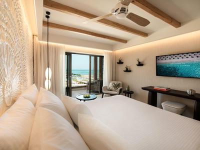 Hell eingerichtetes Schlafzimmer mit großem Bett, Holzdecke, Fenster mit Meerblick und Fernseher an der Wand.