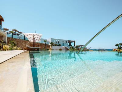 Klare Poollandschaft mit blauem Wasser, Sonnenschirmen, weißen Gebäuden und hellem Himmel.