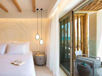 Helles Schlafzimmer mit weißem Bett, runden Pendelleuchten und Terrasse mit Sitzplatz und Blick ins Grüne.