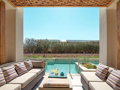 Gemütliche Terrasse mit zwei Sitzgruppen, Glasgeländer und Blick auf Pool und Garten unter blauem Himmel.