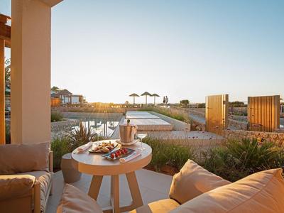 Terrassenbereich mit Holztisch, bequemen Sitzmöbeln und Blick auf Wasser und Hausdächer im Sonnenlicht.