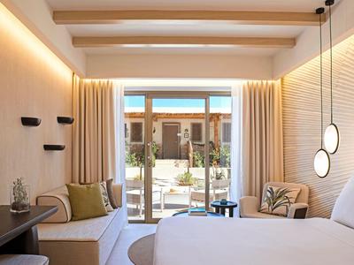 Modernes Hotelzimmer mit Doppelbett, Sofa, hellen Vorhängen und Blick auf Terrasse.