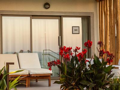 Balkon mit weißen Sitzmöbeln und roten Blumen vor einer geschlossenen Glastür mit Gardinen.