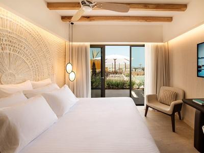 Helles Schlafzimmer mit großem Bett, modernen Lampen, Holzdecke und Blick auf Terrasse durch Glasfenster.