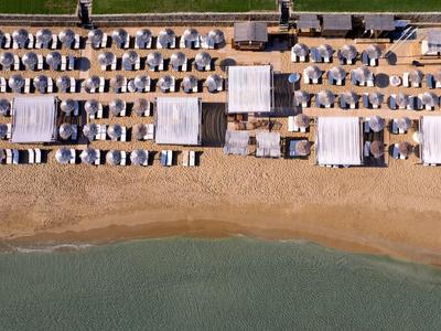 Strand mit vielen Sonnenschirmen und Liegen, neben klarem Wasser und Sandstrand.