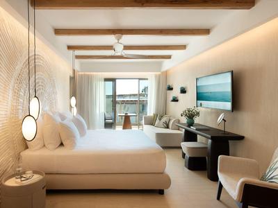 Camera d'hotel moderna con letto matrimoniale, scrivania, sedie e balcone con vista mare.