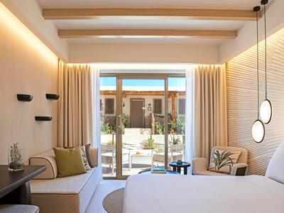 Camera d'hotel moderna con letto grande, divano, piante e terrazza con vista esterna.