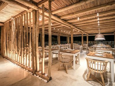 Ristorante aperto con tavoli e sedie in bambù sotto una struttura in legno illuminata caldamente