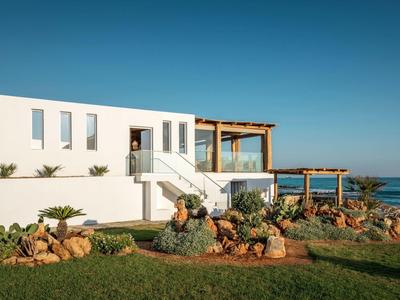 Edificio moderno bianco con terrazza e giardino vicino al mare sotto un cielo limpido.