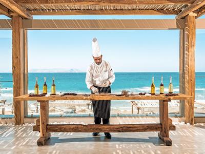 Cuoco sotto un padiglione di legno vicino al mare, con vista sulla spiaggia e sull'acqua blu.
