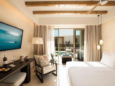 Camera d'hotel moderna con letto grande, TV e accesso a una terrazza con zona salotto.