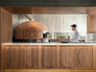 Cuoco prepara cibo in cucina moderna con forno per pizza color rame.