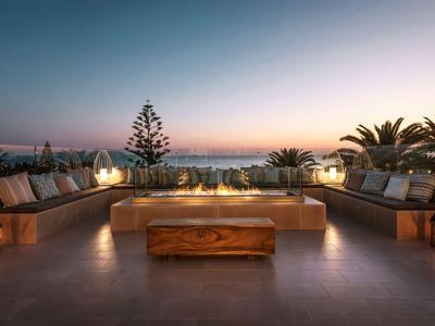 Pohodlná terasa s dřevěným stolem s výhledem na západ slunce a světla města.