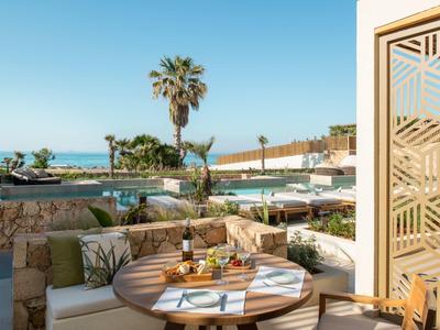 Terrazza dell'hotel con tavolo, sedie e vista sulla piscina, palme e mare sullo sfondo