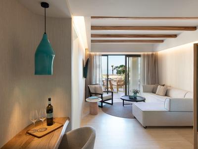 Soggiorno moderno con divano bianco, tavolo da pranzo, lampada a sospensione e accesso al balcone con vista mare.