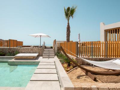 Piscina esterna moderna con sdraio e ombrellone accanto a un edificio in legno.