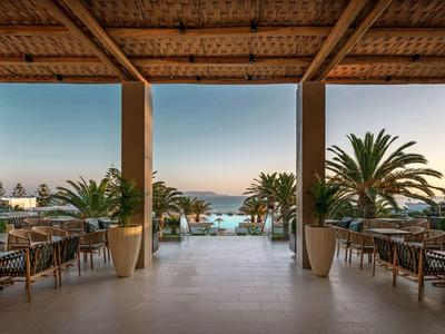 Otevřená jídelna s bambusovým nebo dřevěným stropem s výhledem na palmy a moře při západu slunce.