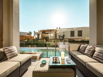 Area salotto con mobili imbottiti che si affaccia su una piscina in un complesso alberghiero alla luce del sole.