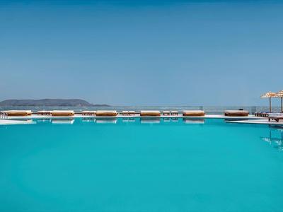 Velký bazén s čistou vodou a slunečníky u moře pod modrou oblohou.