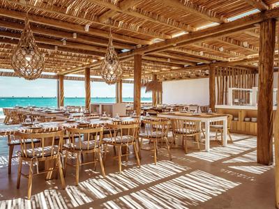 Zona pranzo aperta con soffitto in legno e vista mare in un hotel sulla spiaggia.