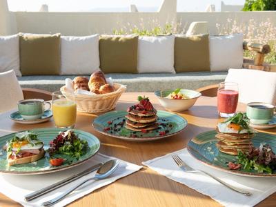 Tavolo per la colazione sulla terrazza con pancake e pane fresco al sole.