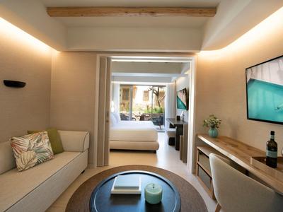 Camera d'hotel moderna con zona salotto, scrivania e vista sulla camera da letto.