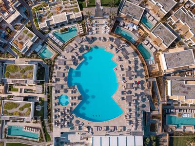 Vista aerea di un hotel con una grande piscina curva e lettini intorno.