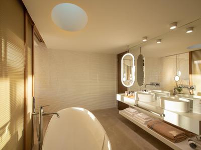 Bagno moderno con vasca da bagno freestanding e doppi lavandini illuminati da luce calda.