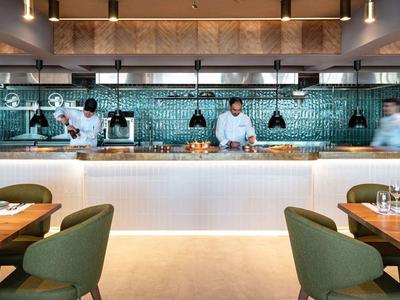 Moderne hotelkeuken met open concept en groene gestoffeerde stoelen in een elegante eetruimte.