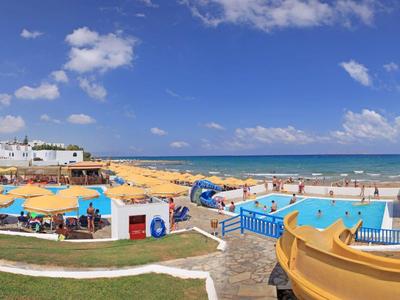 Sonniger Strand mit Pool, Wasserrutschen und bunten Liegestühlen unter blauem Himmel.