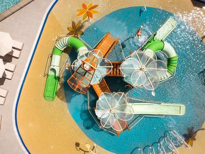Waterpark met glijbanen en zwembad op hotelterrein, omgeven door zandstrand en ligstoelen.