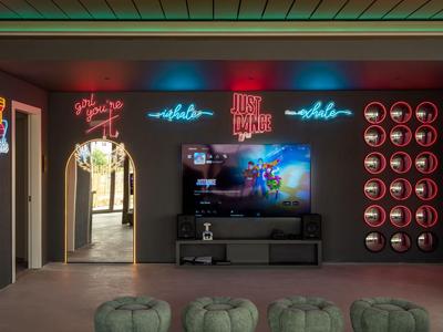 Moderne hotel-lounge met neonlichten, tv en groene kussens.