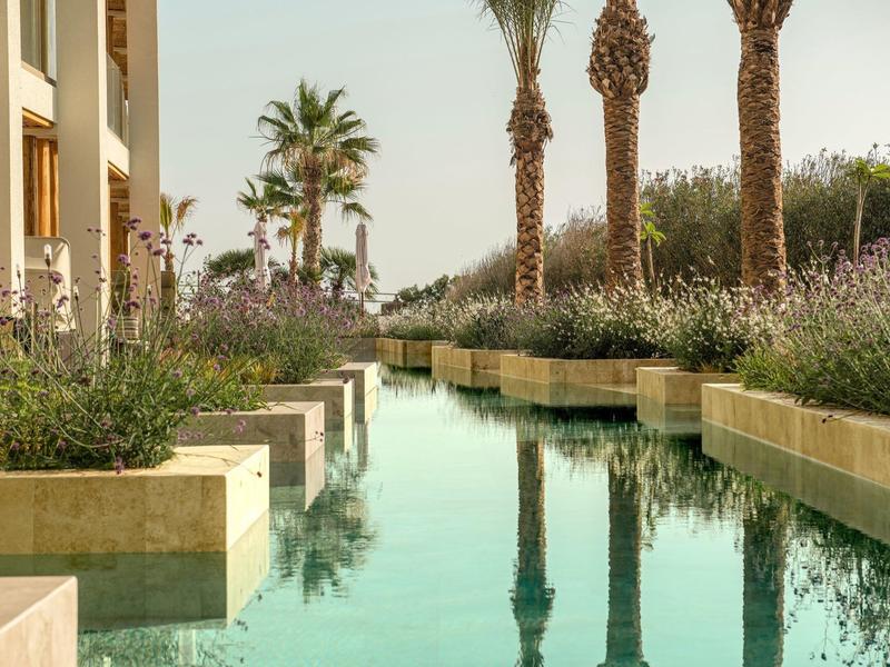 Giardino moderno con specchio d'acqua e palme vicino a un edificio dell'hotel al tramonto.