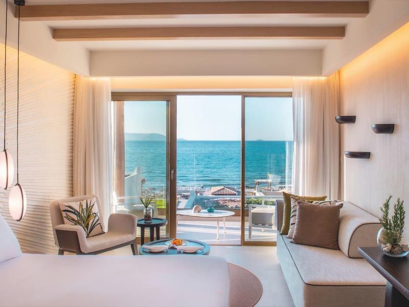 Camera d'hotel moderna con vista sul mare, poltrone accoglienti e ampia finestra.