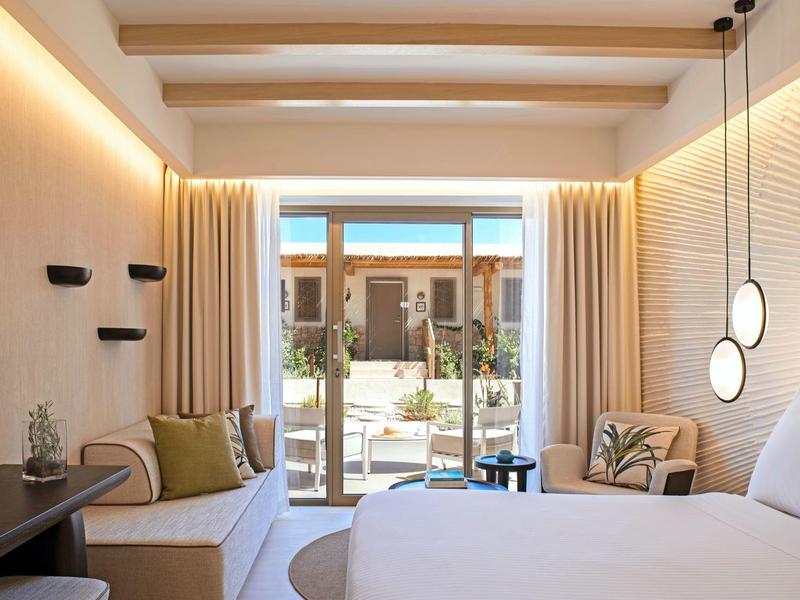 Camera d'hotel moderna con letto grande, divano, piante e terrazza con vista esterna.