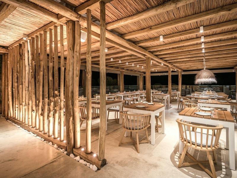Ristorante aperto con tavoli e sedie in bambù sotto una struttura in legno illuminata caldamente