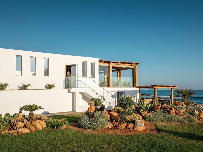 Edificio moderno bianco con terrazza e giardino vicino al mare sotto un cielo limpido.