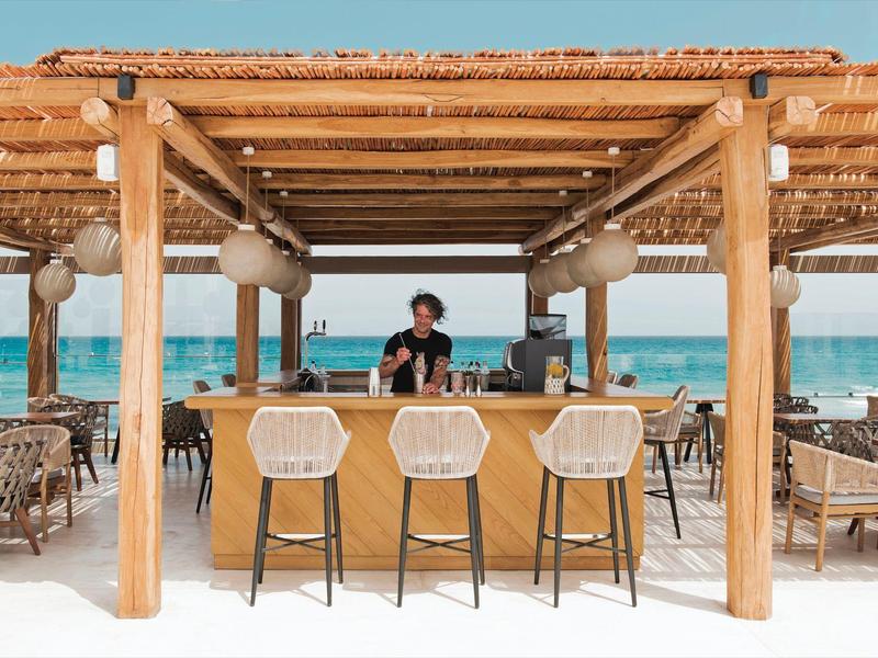 Area bar con sgabelli in rattan sotto un tetto di legno vicino alla spiaggia con vista mare.