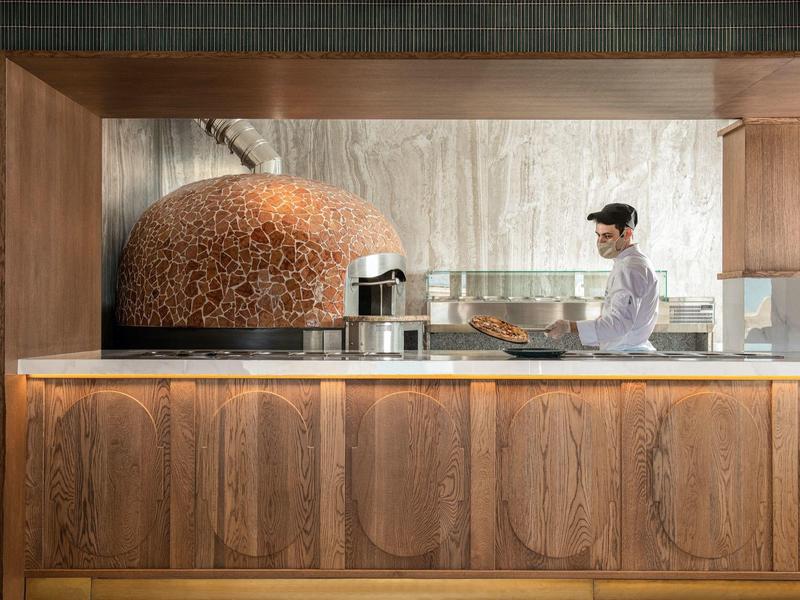 Cuoco prepara cibo in cucina moderna con forno per pizza color rame.