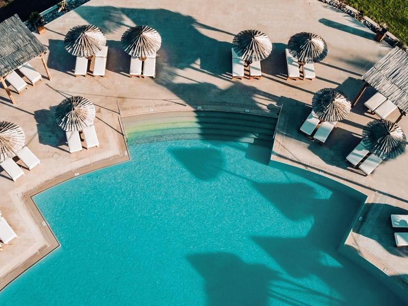 Una piscina a forma di stella con sdraio e tetti in legno intorno, circondata da erba.