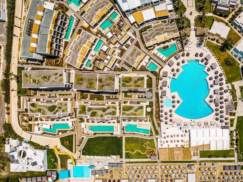 Vista aerea di un resort con più piscine, spiagge e edifici disposti in modo organico.