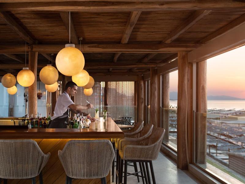 Bar con sgabelli e grandi finestre con vista sul mare al tramonto