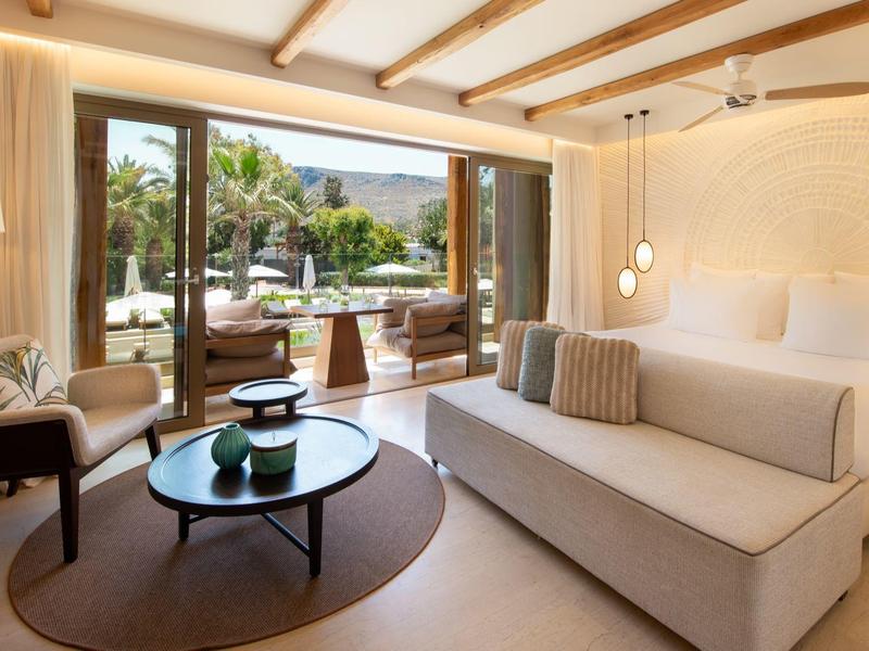 Camera d'hotel moderna con grandi finestre che si affacciano sulla piscina e zona salotto accogliente.