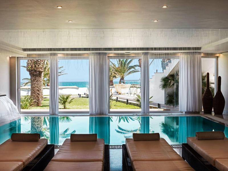 Piscina interna con lettini e vista sulle palme e sul mare attraverso grandi finestre