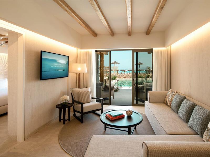 Soggiorno luminoso con divano, poltrona, TV e vista su balcone e mare.