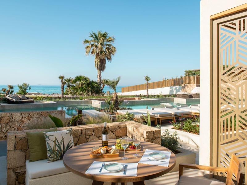 Terrazza dell'hotel con tavolo, sedie e vista sulla piscina, palme e mare sullo sfondo