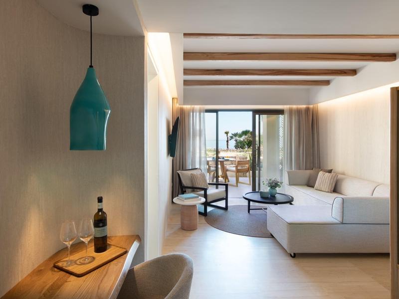 Soggiorno moderno con divano bianco, tavolo da pranzo, lampada a sospensione e accesso al balcone con vista mare.