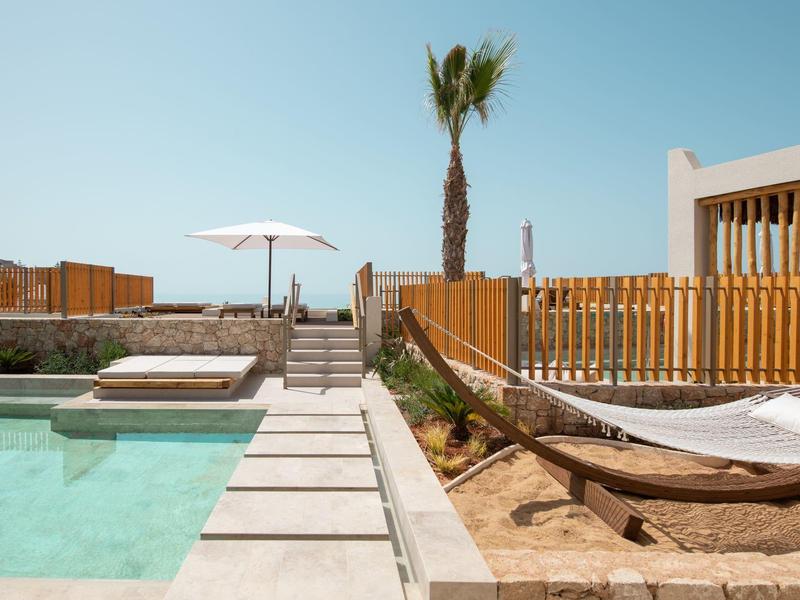 Piscina esterna moderna con sdraio e ombrellone accanto a un edificio in legno.