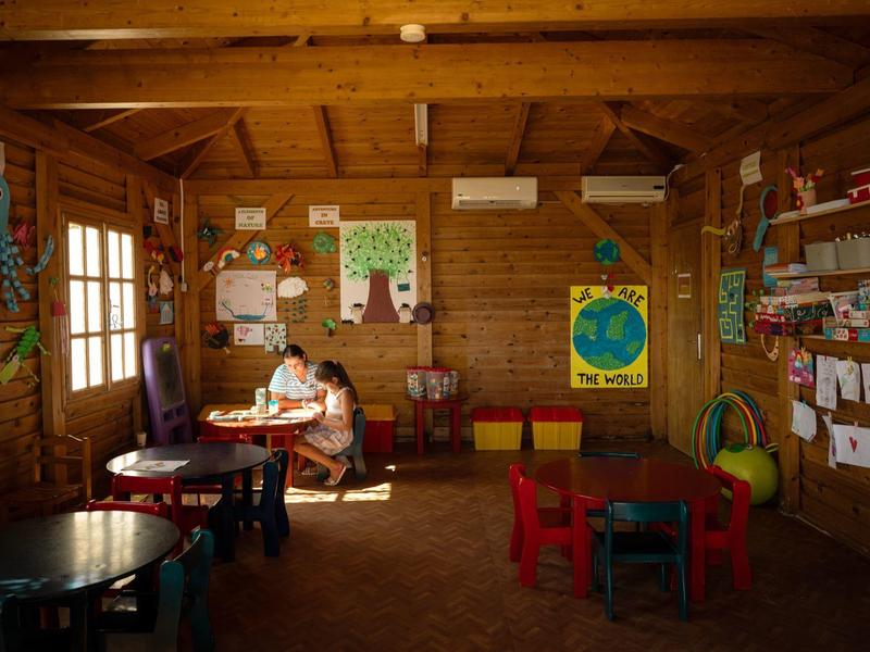 Accogliente stanza in legno con tavoli e sedie per bambini e materiali per lavori manuali alla luce naturale.