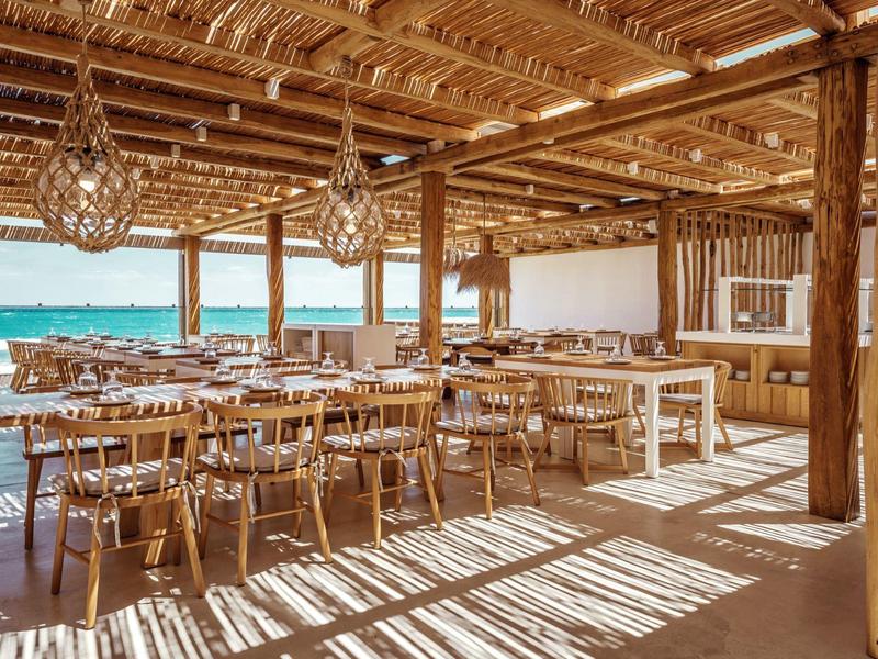 Zona pranzo aperta con soffitto in legno e vista mare in un hotel sulla spiaggia.